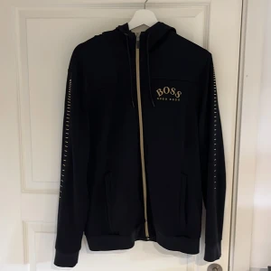 Svart hoodie från Hugo Boss med dragkedja - Svart hoodie från Hugo Boss. Äldre modell säljs inte mer. Det är storlek L men passar även M