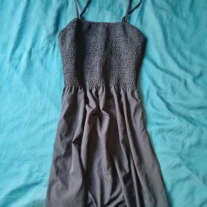 Kort sommarklänning med smock - Klänning med smala axelband och smockad överdel. Kjolen är lätt utställd och tyget känns mjukt och luftigt, perfekt för varma dagar. Enkel och stilren design som är lätt att matcha med accessoarer.