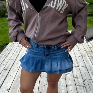 Jeanskjol med volang från U.S. Polo Assn. - Superfin blå jeanskjol från U.S. Polo Assn. med volangkant nertill. Klassisk femficksmodell, bälteshällor och broderad logga i midjan. Kjolen är kort och har en snygg, avslappnad vibe som passar perfekt till sneakers eller boots. Midje: 36-37cm och längd: 35cm 