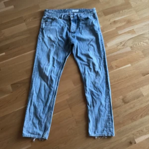 Ljusblå jeans från Tiger of Sweden - Säljer ett par ljusblå jeans från Tiger of Sweden med klassisk femficksdesign och råa, fransiga benslut. Jeansen har raka ben och normal passform, tillverkade i mjuk bomullsdenim. Perfekta för en avslappnad och stilren look.