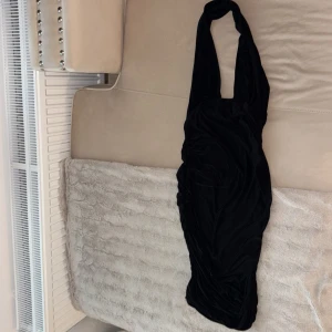 Svart halterneck sammetsklänning - Supersnygg svart sammetsklänning med halterneck och rynkade sidor. Klänningen har en tight passform och är perfekt för dig som vill sticka ut med en elegant och trendig look. Mjuk och följsam känsla tack vare sammetstyget. Väldigt stretchig , en L får på sig den.