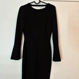 Svart långärmad klänning Gina Tricot - Supersnygg svart klänning från Gina Tricot i figurnära modell. Långärmad med utsvängda ärmslut och djup v-ringning i ryggen. Perfekt för dig som gillar stilrena och trendiga plagg. Materialet känns mjukt och stretchigt. Storlek XS. Den är använd fåtal gånger, så den är som ny.