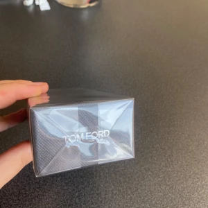 Tom Ford Oud Wood EdP 100ml - Tom Ford Oud Wood Eau de Parfum 100 ml i elegant mörkgrå kartong med svart etikett och silverdetaljer. Lyxig och ikonisk doft med träiga och kryddiga toner, perfekt för dig som gillar exklusiva parfymer. Flaskan är förseglad i plast.