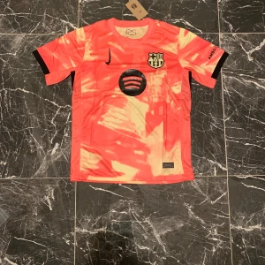 Barcelona x Nike kortärmad fotbollströja S - Säljer en Barcelona x Nike fotbollströja i storlek S. Tröjan är kortärmad med en unik orange och ljusgul batikliknande design, svarta detaljer och klubbmärke på bröstet. Materialet är lätt och andas, perfekt för träning eller match. Spotify-logga på framsidan.