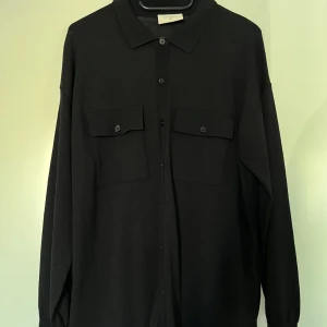 Svart skjorta, Free/Quent, L - Svart skjorta från Free/quent med långa ärmar, krage och knappstängning framtill. Den har två bröstfickor med knappar. Skjortan har en avslappnad passform. 60% polyester och 40% viskos. Skjortan är i nyskick.  Mått: Längd ca 68 cm Byst ca 53 cm Midja ca 53 cm Ärmlängd mätt från axeln ca 51 cm Axel till axel ca 55 cm