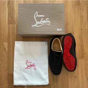 Svarta sneakers från Christian Louboutin - Snygga svarta sneakers från Christian Louboutin med klassisk röd sula och diskret logga på insidan. Skorna har rund tå, snörning och är tillverkade i skinn. Perfekta för dig som vill ha en exklusiv och stilren look.