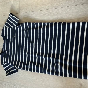 Randig klänning från GANT - Säljer en stilren randig klänning från GANT i marinblått och vitt. Perfekt för en avslappnad look. Klänningen har korta ärmar och är tillverkad i mjukt bomullsmaterial. Passar perfekt för både vardag och fritid.