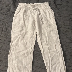 Vita linnebyxor med knytband - Snygga vita linnebyxor med elastisk midja och dekorativt knytband. Byxorna har en avslappnad passform och är perfekta för varma dagar. De har praktiska fickor på sidorna och en luftig design. OPS, de finns ett hål i mellan benen men syns knappt när dom sitter på! 