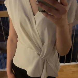 Zara blus - Säljer en elegant vit omlottblus med korta ärmar och knytning i midjan. Perfekt för en stilren look. Blusen har en v-ringad design som ger en feminin touch.