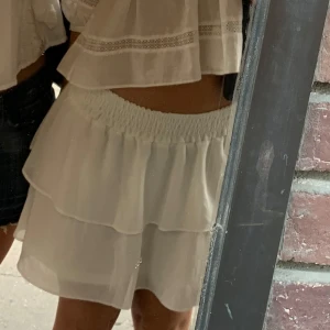 Vit volangkjol - Söt vit kortkjol med volanger. Kjolen har en elastisk midja för en bekväm passform och är perfekt för varma dagar 🩷 