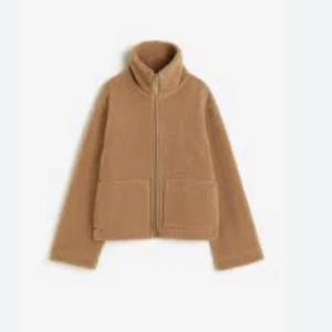 Beige teddyjacka med dragkedja - Mysig beige teddyjacka med dragkedja och hög krage. Jackan har två stora fickor framtill och långa ärmar. Perfekt för kyliga dagar.