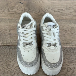 Vita och silver sneakers från Juicy Couture - Snygga vita sneakers från Juicy Couture med glittrande silverdetaljer och snörning. Perfekta för att ge din outfit en extra touch av glamour. Märkeslogga på plösen och sidan. Nästintill Nya ❤️
