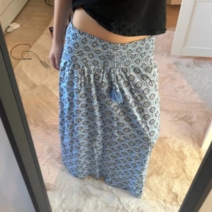 Blå mönstrad kjol från Gina Tricot - Säljer en blå långkjol från Gina Tricot med ett snyggt mönster i mörkblått och vitt. Kjolen har en elastisk midja och dekorativa tofsar framtill. Perfekt för sommaren😀