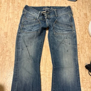 Low waist jeans från Hilfiger Denim - Snygga blå jeans från Hilfiger Denim med en klassisk femficksdesign och slitna detaljer. Byxorna har en låg midja och bootcut-stil, säljer eftersom att de är för korta, men i perfekt skick! Pris kan diskuteras