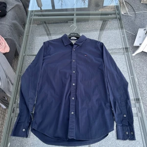 Mörkblå skjorta från Tommy Jeans - Snygg mörkblå skjorta från Tommy Jeans i slim fit. Skjortan har långa ärmar och knappar framtill. Den är tillverkad i ett mjukt material och har en liten broderad logga på bröstet. Perfekt för en stilren look.