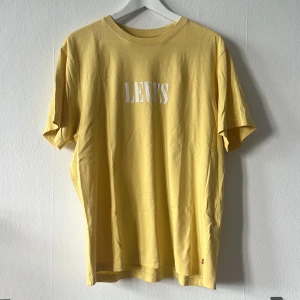 Gul t-shirt från Levi's - Säljer en gul t-shirt från Levi's med vit logga på bröstet. T-shirten har en avslappnad passform och är tillverkad i bomull. Perfekt för en casual look. 🌟