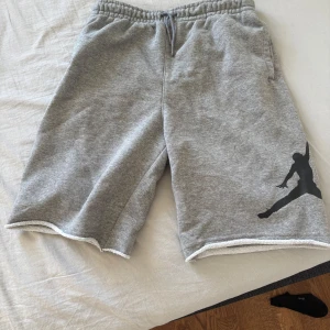 Grå shorts från Jordan - Säljer ett par grå shorts från Jordan med en svart siluett på benet. De har elastisk midja med snörning och är tillverkade i ett mjukt material. Perfekta för en avslappnad stil. Har använt de ändå ganska mycket. Det är bara att höra av dig om du undrar något😀