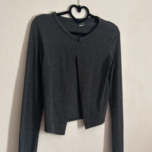 Grå kofta från Gina Tricot - Säljer en stilren grå kofta från Gina Tricot. Den har en enkel knapp framtill och långa ärmar. Perfekt för lager-på-lager-stil. 🖤