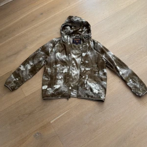 Camouflage vindjacka från Woolrich - Säljer en cool vindjacka från Woolrich i ett unikt camouflage-mönster. Storlek L, Jackan har en dragkedja framtill och en praktisk huva. Perfekt för vår och höst när vädret är oförutsägbart. 