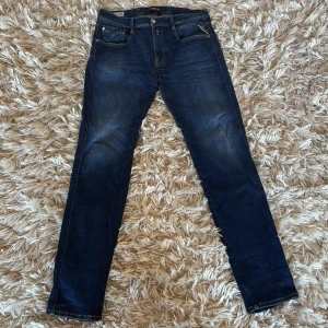 Replay Anbass 32/32 - Snygga mörkblå jeans från Replay, modell Anbass. De har en slim fit passform och är tillverkade i ett återvunnet material. Klassisk design med fem fickor och dragkedja. Perfekta för en stilren look.