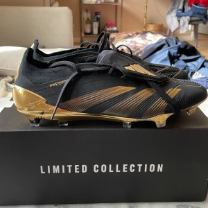 Svarta och guldiga fotbollsskor från Adidas - Snygga fotbollsskor från Adidas i svart och guld. Skorna har en modern design med snörning och en elegant guldig sula. Perfekta för den som vill sticka ut på planen. Sällsynta Bellingham fotbollskor i bra skick 