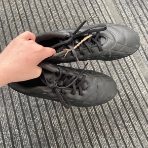 Svarta fotbollsskor med dobbar - Säljer ett par svarta fotbollsskor med snörning och dobbar för bra grepp på planen. Skorna har en stilren design och är perfekta för fotbollsträning eller match. Det behövs bara tvättas lite så är den bra