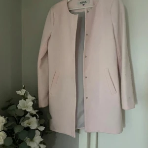 Ljusrosa kappa från ONLY - Säljer en stilren ljusrosa kappa från ONLY. Den har en enkel design med knappar framtill och två fickor. Perfekt för vår och höst. I mycket fint skick. Storlek S, normal i storlek 