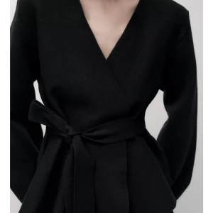 Svart omlottjacka från Zara - Elegant svart omlottjacka från Zara med knytband i midjan. Jackan har en v-ringad design och långa ärmar, vilket ger en stilren och modern look. Perfekt för att ge en sofistikerad touch till din outfit.