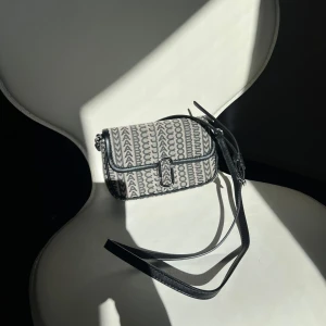 Marc Jacobs axelremsväska  - Snygg marc Jacobs väska i svart och grått. Väskan har en justerbar rem och ett spänne framtill. Perfekt för att ge din outfit en stilfull touch. Använd endast 1 gång, dustbag medkommer. 