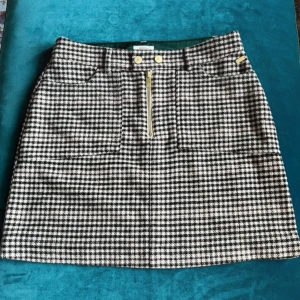Rutig kjol från Scotch & Soda - Snygg rutig kjol från Scotch & Soda i en brun/beige färg med dragkedja fram och två knappar i midjan. Kjolen har en klassisk design med fickor fram och är perfekt för en stilren look. Finns reserv-knappar till. 