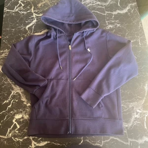 Mörkblå hoodie från Ralph Lauren - Säljer en snygg mörkblå hoodie från Ralph Lauren med dragkedja och huva. Den har en liten broderad logga på bröstet och praktiska fickor framtill. Perfekt för en avslappnad stil. Fickan gick av men jag sydde den. Men om nån som kan sy den bra så ser det ut som normal igen.