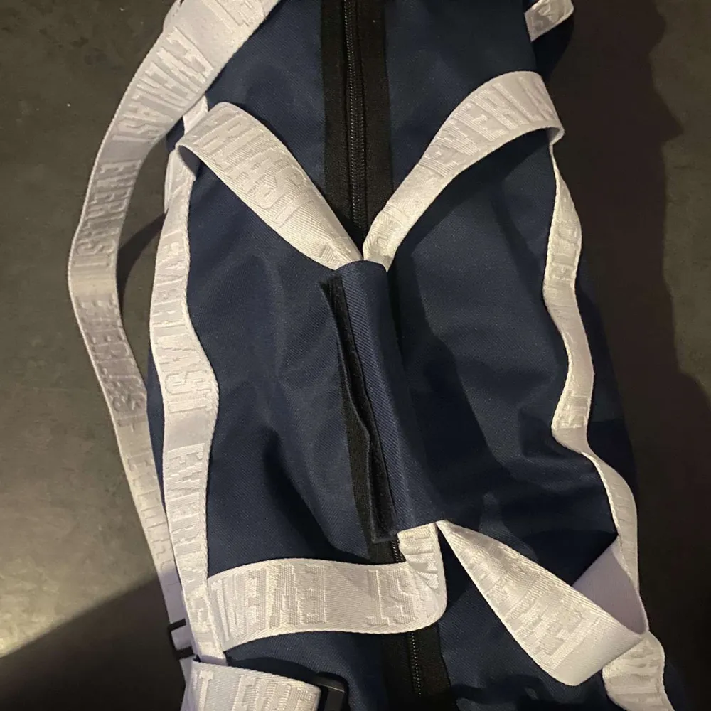 Säljer en blå träningsväska från Everlast med vita detaljer och logotyp. Väskan har en justerbar axelrem och bärhandtag. Laukut & Käsilaukut.