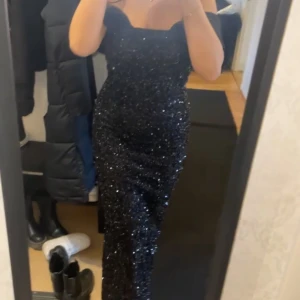 Svart glittrig långklänning - Säljer en elegant svart långklänning med glittrande paljetter. Klänningen har en tight passform och är axelbandslös, perfekt för festliga tillfällen. Den har en slits som ger extra rörelsefrihet.