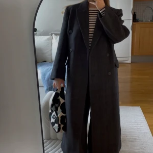 Grå rutig kappa weekday  - Säljer en elegant grå rutig kappa med dubbelknäppning. Den har en klassisk design med långa ärmar och en rak passform. Perfekt för att hålla stilen under kyligare dagar.