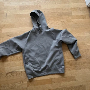 Grå hoodie - Säljer en stilren grå hoodie med normal passform. Den har en klassisk design med huva och långa ärmar. Perfekt för en avslappnad look.