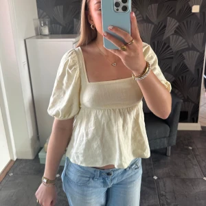 Ljusgul topp med öppen rygg - Säljer en söt ljusgul blus från H&M i storlek S med puffiga kortärmar och öppen rygg med knytband. Superbra för varmare dagar och passar till allt.