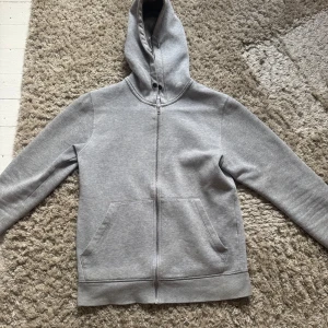Grå hoodie med dragkedja  - Säljer en stilren grå hoodie med dragkedja och fickor framtill. Perfekt för en avslappnad look. Den har en bekväm passform och en praktisk huva. Tröjan är från Jack n jones 