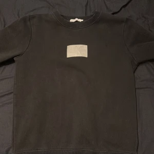 Svart tröja från Calvin Klein Jeans - Säljer en stilren svart tröja från Calvin Klein Jeans med en grå logotyp på bröstet. Tröjan har långa ärmar och en rund halsringning med ribbade kanter. Perfekt för en avslappnad look.