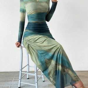 Grön och blå långklänning - Snygg långklänning i gröna och blå toner med ett unikt mönster. Klänningen har långa ärmar och en smickrande drapering i midjan som ger en elegant siluett. Perfekt för en stilfull look. Använd 1-2 gånger.