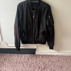 Svart bomberjacka från ONLY - Snygg svart bomberjacka från ONLY med dragkedja framtill och på ärmen. Jackan har långa ärmar och ribbade muddar vid ärmslut och nederkant. Perfekt för en cool och avslappnad stil.