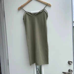 Pull & Bear grön klänning, storlek M - Säljer en stilren olivgrön klänning med smala axelband. Klänningen har en enkel design och är perfekt för varma dagar. Den är tillverkad i ett mjukt material som ger en bekväm passform.