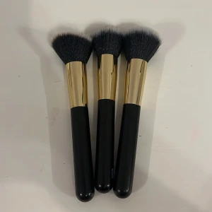 Set med tre sminkborstar - Säljer ett set med tre sminkborstar med svarta handtag och guldfärgade detaljer. Borstarna har mjuka, täta borst i olika former för applicering av smink. Perfekt för både nybörjare och proffs. En sminkborstän är lite använde, men de två andra är helt oanvända.Men även om den ena är lite använd funkar den lika bra.