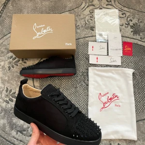 Svarta Christian Louboutin - Snygga svarta sneakers från Christian Louboutin med ikoniska röda sulor och nitar på tån. Skorna har snörning och är tillverkade i skinn, vilket ger en lyxig känsla. Perfekta för att ge din outfit en edgy touch.
