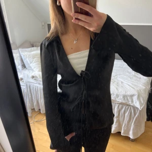 Svart långärmad blus med knyt - Snygg svart blus i satin med långa ärmar och knytning framtill. Toppen är aldrig använd med prislapp kvar🥰