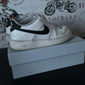 Nike Air Force 1 i vitt och svart - Säljer ett par klassiska Nike Air Force 1 sneakers i vitt med svart swoosh. Skorna har en rund tå och snörning framtill. Perfekta för en stilren och sportig look. Tvättas rejält innan jag fraktar dom 