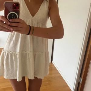 Vit klänning  - Söt vit kortklänning med v-ringning och spetsdetaljer. Klänningen är ärmlös, har volang nertill och en luftig passform. Perfekt för varma dagar, student, konfirmation och somriga tillfällen.