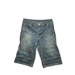 Sarahbrand jorts - Säljer ett par blå jeansshorts från Sarahbrand med klassisk femficksdesign och broderad logga på benet. Shortsens modell är loose fit och de har normalhög midja. Perfekta för sommaren och har snygga detaljer som märkets patch och brodyr. Som du ser har jag vikt upp änderna av jortsen som har lett till flera vikningar.