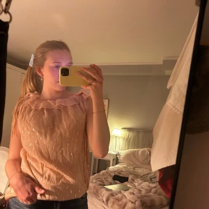 Rodebjer blus - Söt beige rosa blus med volangdetalj vid halsringningen och diskret prickigt mönster. Blusen är ärmlös och har en luftig passform, perfekt för varmare dagar.
