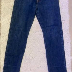 Levi's 501 blå jeans storlek W27 L30 - Klassiska blå Levi's 501 jeans med raka ben och femficksmodell. Jeansen har knappgylf och den ikoniska läderpatchen bak i midjan. Perfekta för en tidlös och avslappnad stil. Storlek ligger på W27 L30