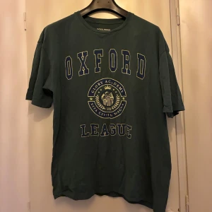 Grön Oxford League t-shirt - Säljer en grön t-shirt från jack & Jones med tryck i vitt och gult framtill där det står 'Oxford League'. T-shirten har rund hals och korta ärmar, perfekt för en avslappnad stil.